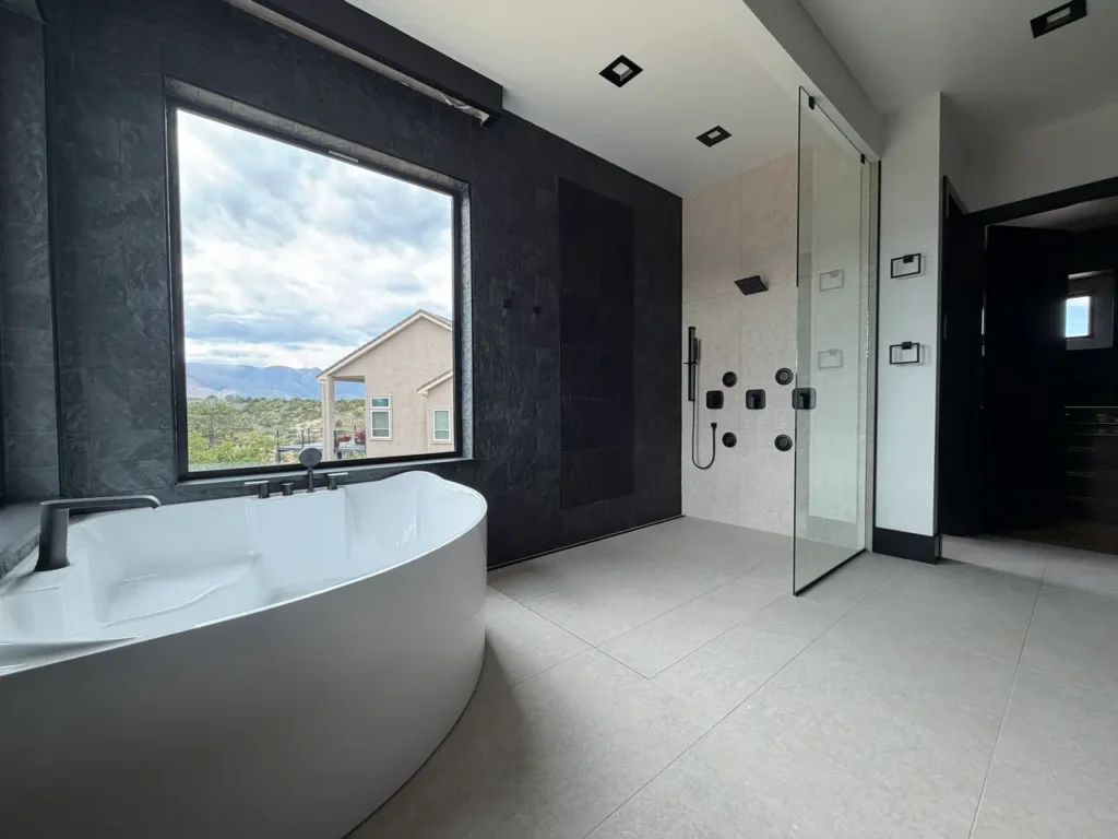 Open-concept luxury master bathroom featuring a curbless walk-in shower, dark textured slate accent walls, and a freestanding tub.