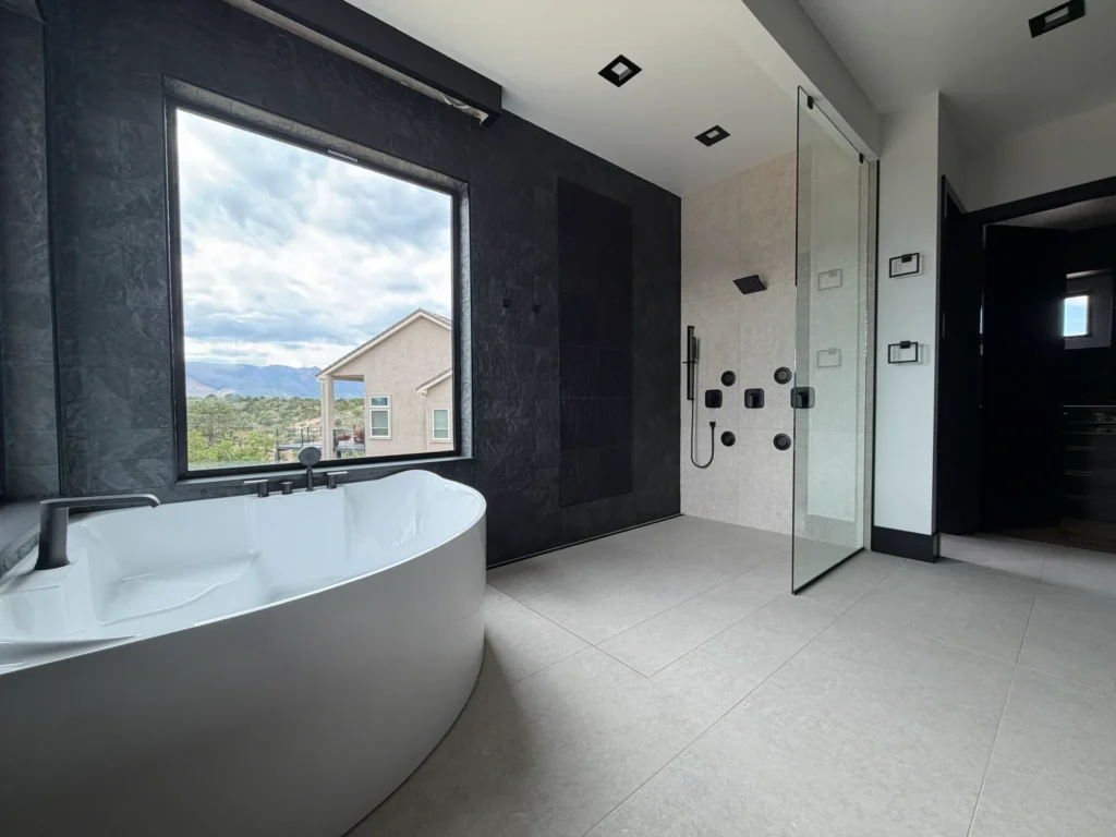 Open-concept luxury master bathroom featuring a curbless walk-in shower, dark textured slate accent walls, and a freestanding tub. Custom Tile Installation Cost Colorado Springs | XCEL TILE