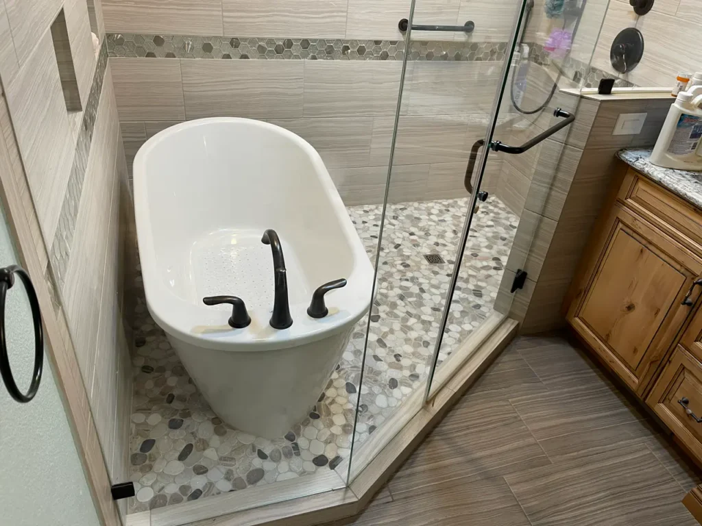 Close-up of a modern freestanding tub and glass shower enclosure in a custom wet room in The Broadmoor featuring textured neutral tiles by XCEL TILE.