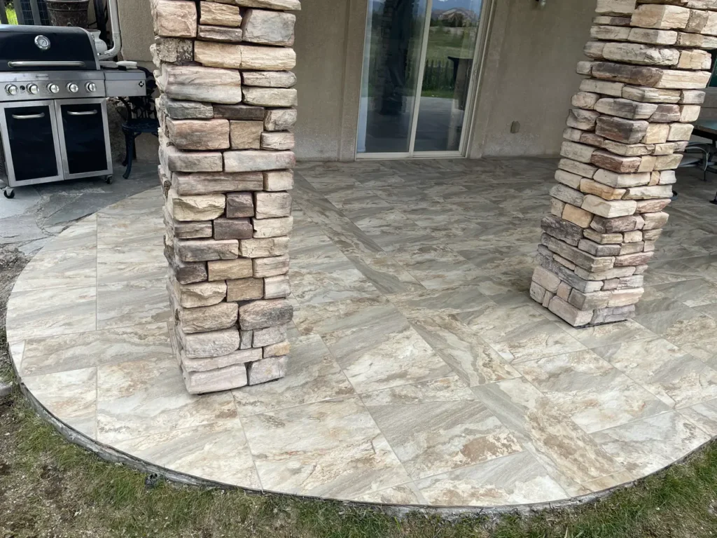 Close-up of large-format outdoor stone-look porcelain patio tiles in Peyton, CO, meeting custom stacked stone support columns by XCEL TILE.