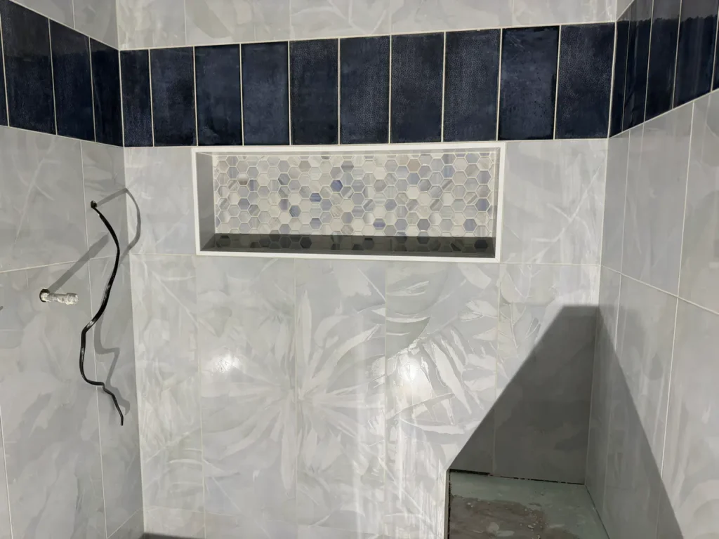 Close-up of a custom wide shower niche filled with hexagon mosaic tiles, positioned seamlessly below a band of dark navy vertical accent tiles in Manitou Springs, CO, by XCEL TILE.