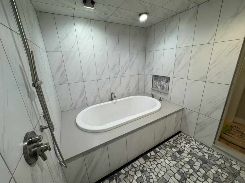 Luxury wet room interior highlighting a freestanding bathtub built into a raised marble-look porcelain tile deck. XCEL TILE - Custom Wet Room Installation Colorado Springs