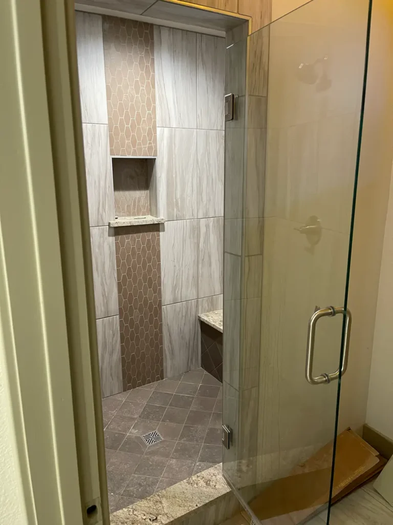Finished walk-in shower featuring light wood-look wall tile, a vertical accent band of brown hexagon mosaics, a built-in niche, a bench, and a diagonally set stone-look floor in Parker, CO, by XCEL TILE.