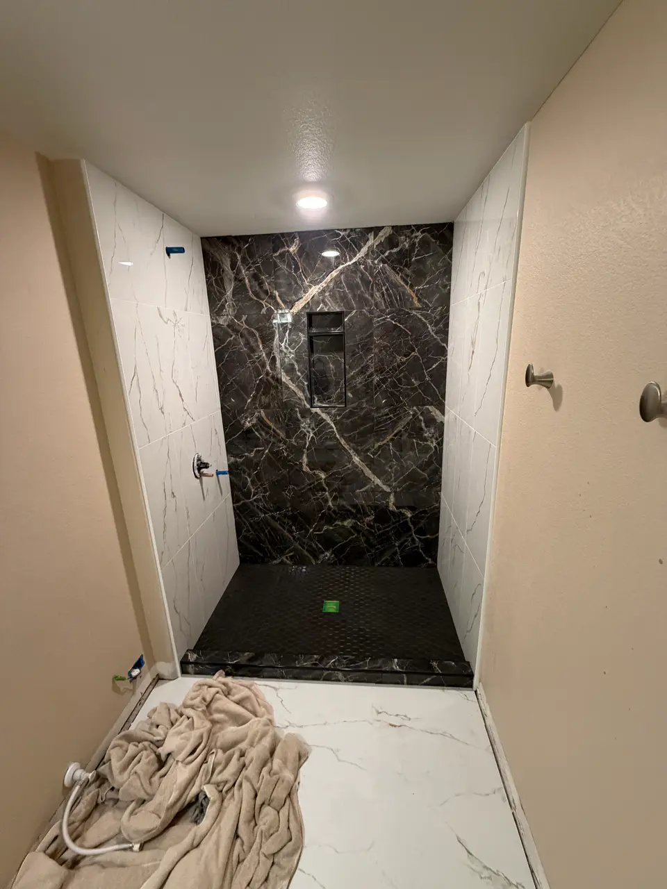 Luxury walk-in shower tile installation featuring large-format white marble-look walls, a dark veined accent wall, and black hex floor pan.