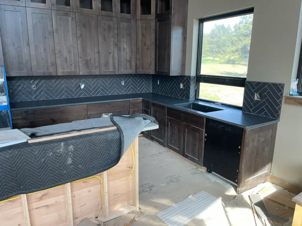 Complete kitchen in Black Forest, CO, featuring dark wood cabinetry and a sweeping dark grey herringbone pattern tile backsplash by XCEL TILE.
