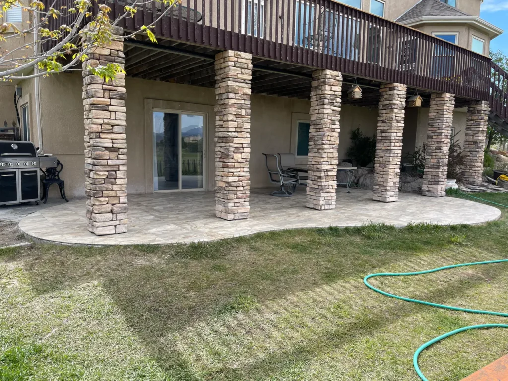 Wide view of a large covered outdoor patio in Peyton, CO, finished in durable stone-look porcelain floor tiles beneath a wooden deck by XCEL TILE.