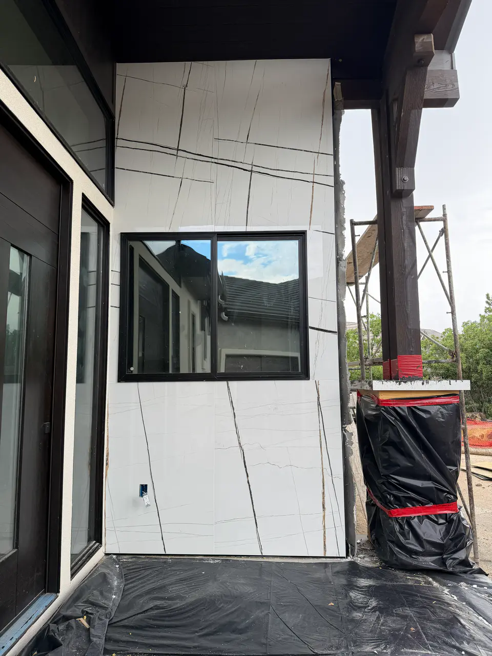 Close-up of exterior facade construction featuring white marble-look porcelain slabs meticulously cut and wrapped around a black window frame.