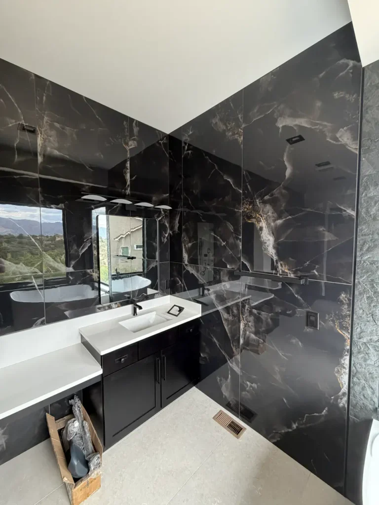 Luxury bathroom featuring full-height dark marble-look gauged porcelain wall panels with striking gold veining. XCEL TILE - Custom Tile Services Colorado Springs