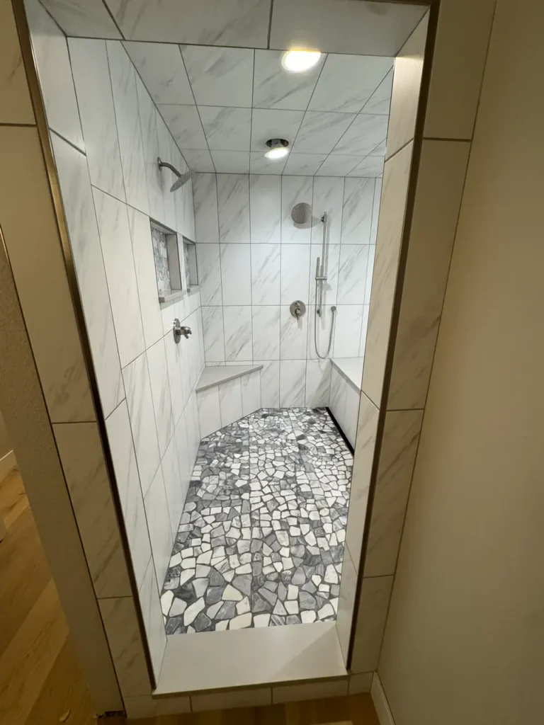 View through a doorway into a luxury wet room showcasing a fully tiled marble-look ceiling and custom pebble shower floor. XCEL TILE - Custom Tile Services Colorado Springs