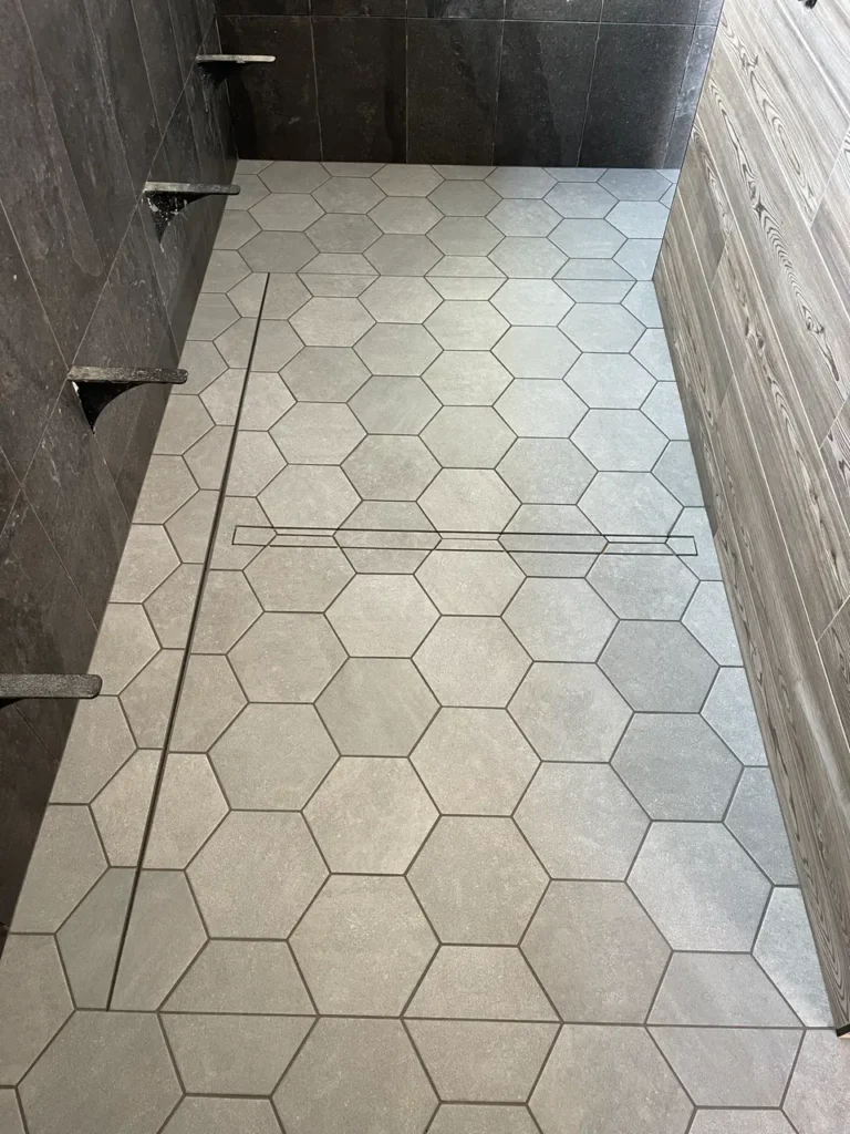 Completed large walk-in shower floor in Castle Rock, CO, featuring light grey hexagon tiles perfectly sloped toward a sleek linear drain by XCEL TILE.