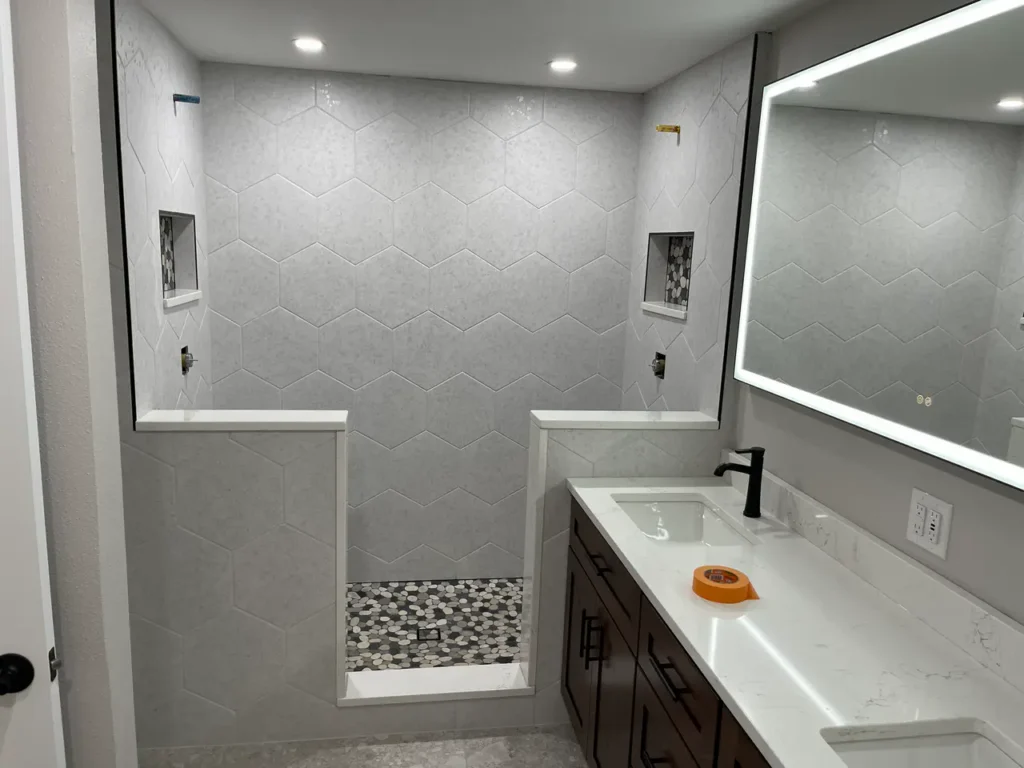 Modern master bathroom in Woodland Park, CO, featuring a walk-in shower with light grey hexagon wall tiles and a pebble mosaic floor by XCEL TILE.