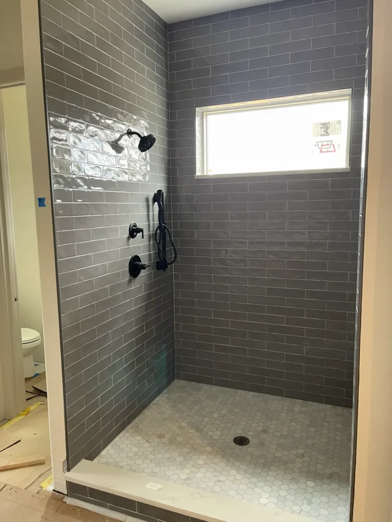 Finished custom walk-in shower in Larkspur, CO, featuring glossy grey subway tile walls, a white marble hexagon mosaic floor pan, and modern matte black fixtures by XCEL TILE.