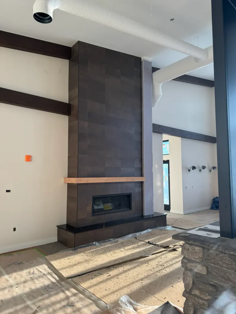 Completed dark stone-look floor-to-ceiling fireplace surround in Monument, CO, with a natural wood mantel in a modern, bright residential living space by XCEL TILE.