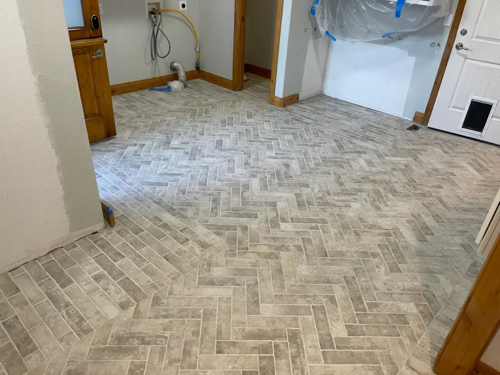 Custom mudroom flooring featuring weathered grey brick-look porcelain tiles installed in a classic herringbone pattern with bordered edges.