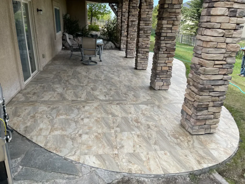 Covered outdoor patio in Peyton, CO, featuring large-format stone-look porcelain tiles and custom stacked stone pillar wraps by XCEL TILE.