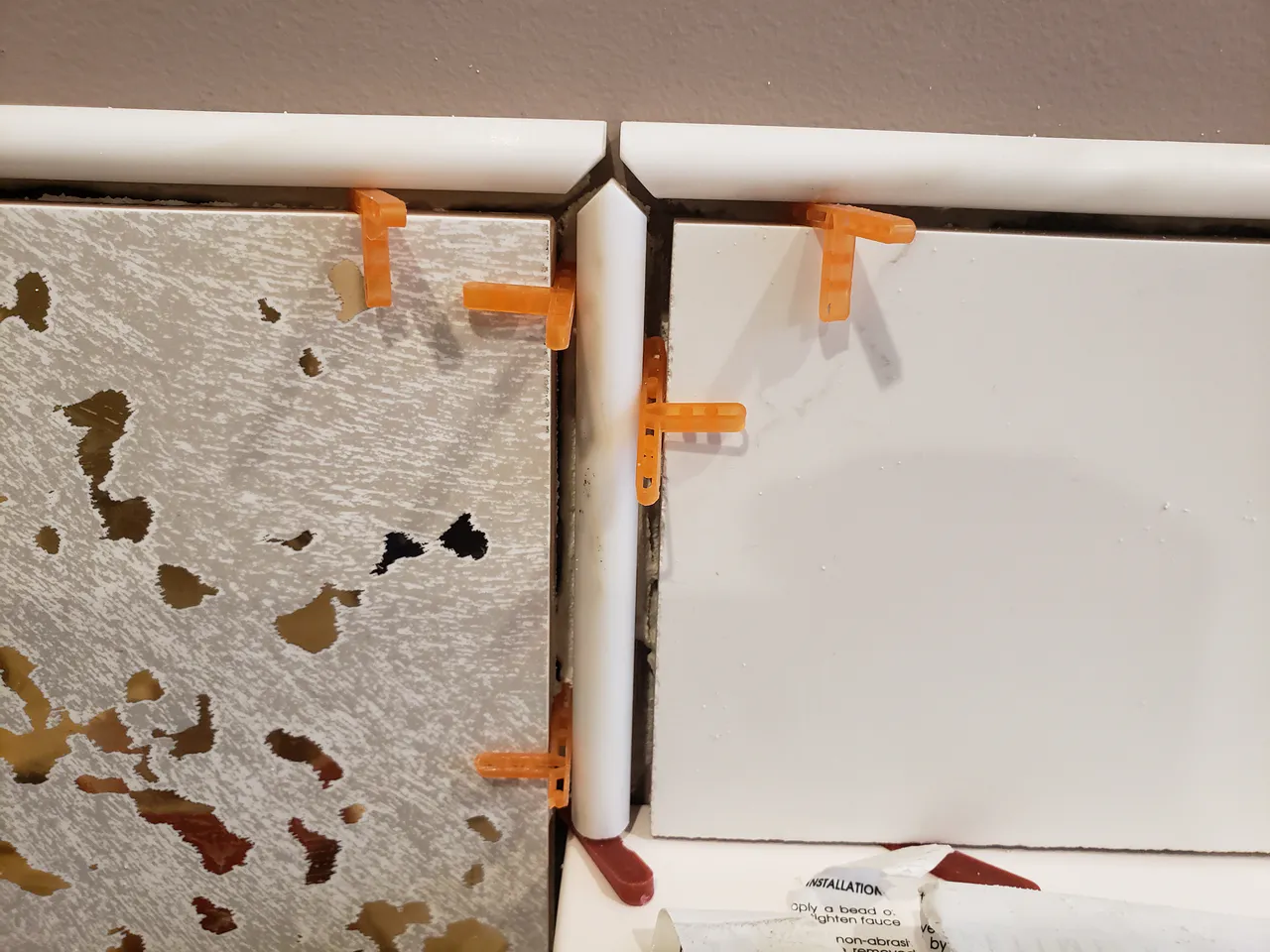 Close-up of a complex three-way tile corner in Parker, CO, being installed, featuring white tile, textured silver tile, and white bullnose trim pieces by XCEL TILE.