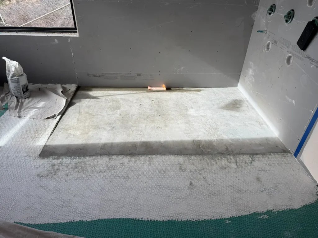 Custom walk-in shower subfloor showing a professionally sloped mortar bed over waterproof membrane preparation.