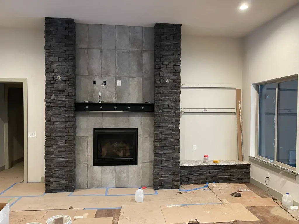 Large custom fireplace under construction in Larkspur, CO, featuring a smooth grey tile center flanked by two floor-to-ceiling columns of dark stacked stone by XCEL TILE.