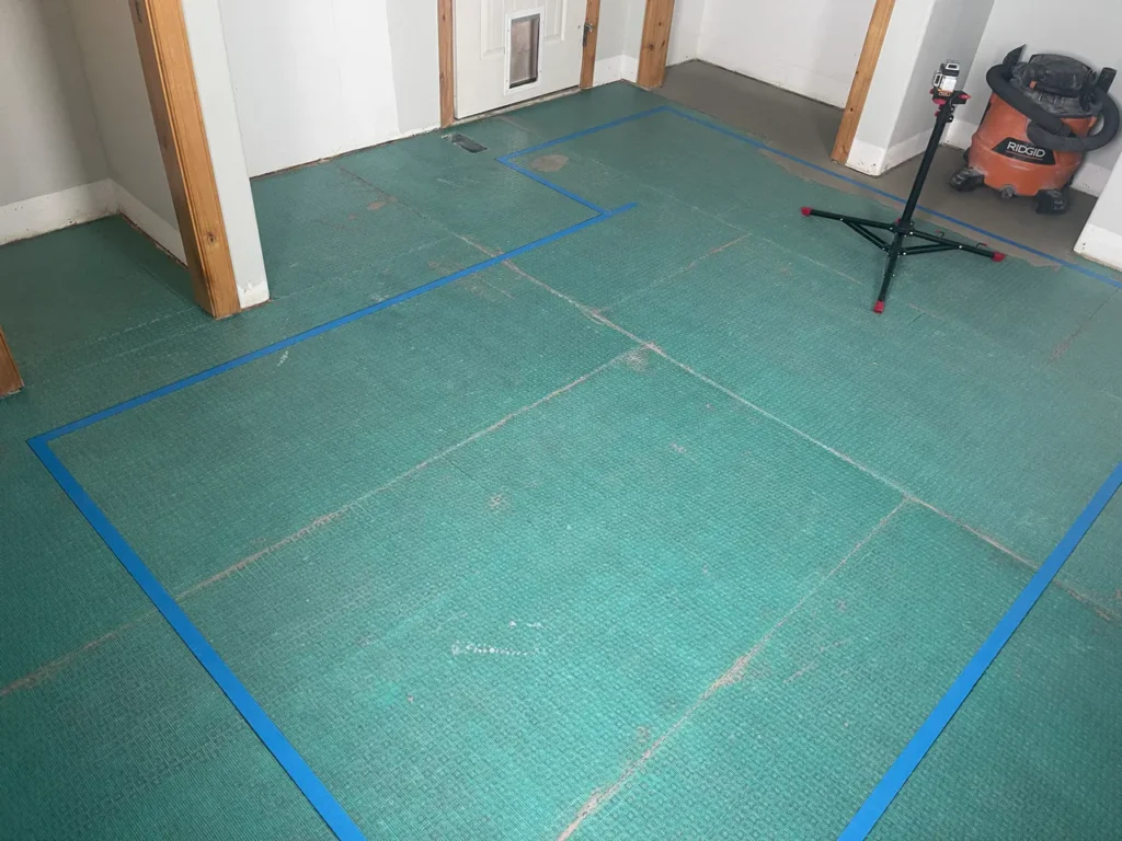 Subfloor preparation showcasing a green uncoupling membrane and blue layout tape for a custom floor tile installation in Colorado Springs, CO, by XCEL TILE.