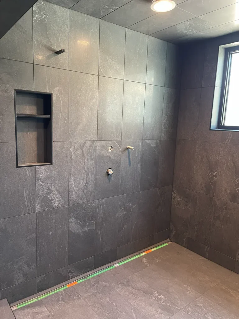 Custom walk-in shower featuring fully tiled charcoal porcelain ceiling, walls, and a built-in multi-tier niche.