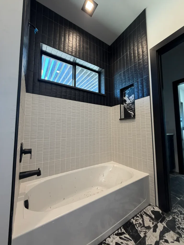 Modern bathtub surround in Colorado Springs, CO, featuring textured white vertical subway tiles on the lower half, bold black vertical subway tiles on top, and a custom recessed niche by XCEL TILE.