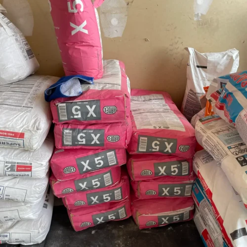Close-up of multiple pink Ardex X 5 polymer modified thin-set mortar bags stacked together in a shop space.