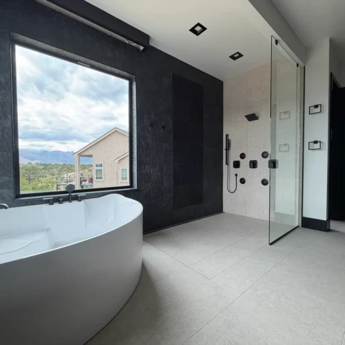 Open-concept luxury master bathroom in Colorado Springs, CO, featuring a curbless walk-in shower, dark textured slate accent walls, and a freestanding tub by XCEL TILE.