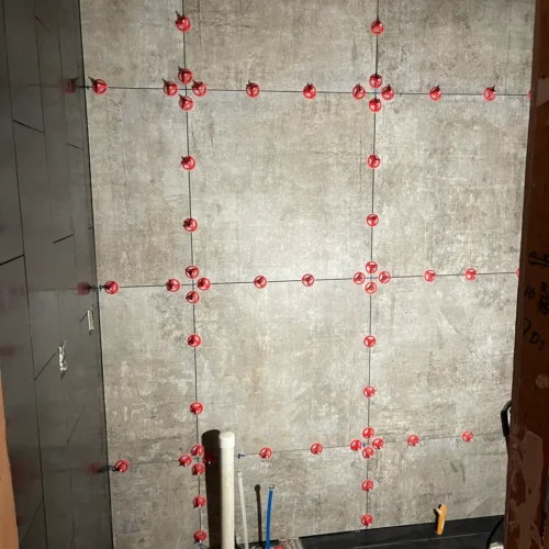 Large format grey bathroom wall tile being installed with red leveling clips by XCEL TILE in Parker, CO.