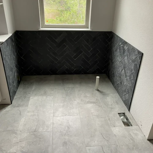 Bathroom nook featuring a highly textured black herringbone tile accent wall installed as wainscoting over light grey stone-look floor tiles in Monument, CO, by XCEL TILE.