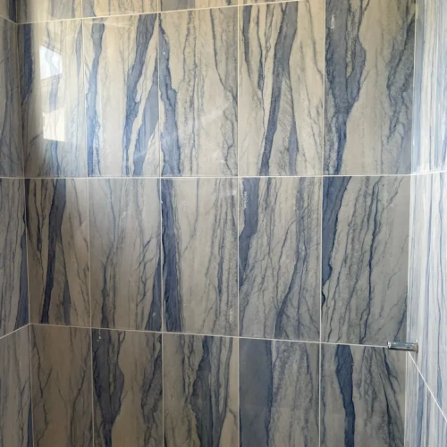 Bathtub and shower surround in Castle Rock. CO, finished in large-format, vertically stacked tile featuring a striking white and deep blue marble-veined pattern by XCEL TILE.