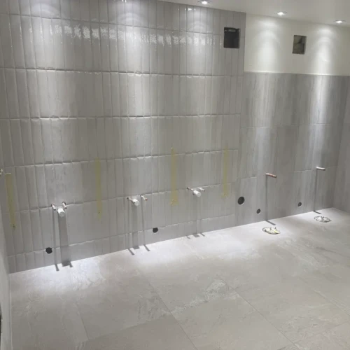 Commercial restroom wall under construction in Colorado Springs, CO, featuring large-format matte grey lower tiles transitioning into glossy vertical accent tiles near the ceiling by XCEL TILE.
