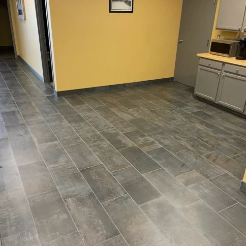 Finished dark grey porcelain floor tile and matching tile baseboards installed in a commercial office breakroom in Colorado Springs, CO, by XCEL TILE.