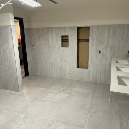 Light grey large-format tile installed on the floors and walls of a commercial restroom, featuring a white multi-sink floating vanity in Colorado Springs, CO, by XCEL TILE.