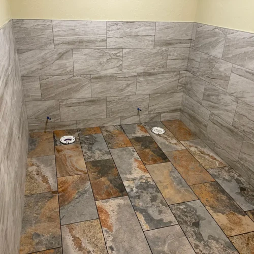 Finished commercial restroom featuring natural slate floor tiles and contrasting grey stone-look wall tile wainscoting in Colorado Springs, CO, by XCEL TILE.