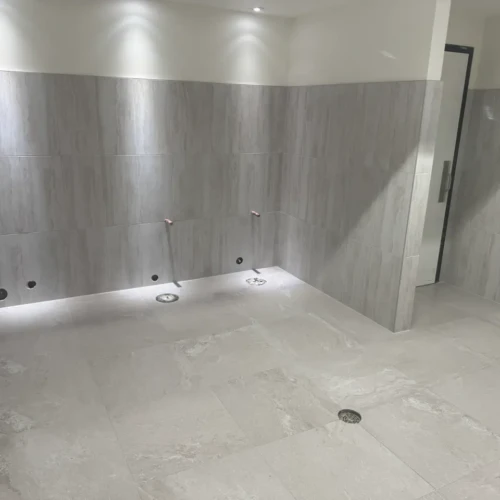 Completed commercial restroom featuring seamless large-format grey stone-look tile on the floors and halfway up the walls in Colorado Springs, CO, by XCEL TILE.