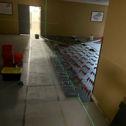 Commercial tile installation in progress in Colorado Springs, CO, utilizing red leveling clips and bright green laser levels across a large office floor by XCEL TILE.