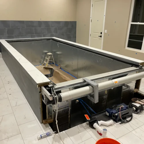 Indoor swimming pool structure featuring dark grey tiled exterior walls surrounded by an expansive white marble-look tile deck in Parker, CO, by XCEL TILE.