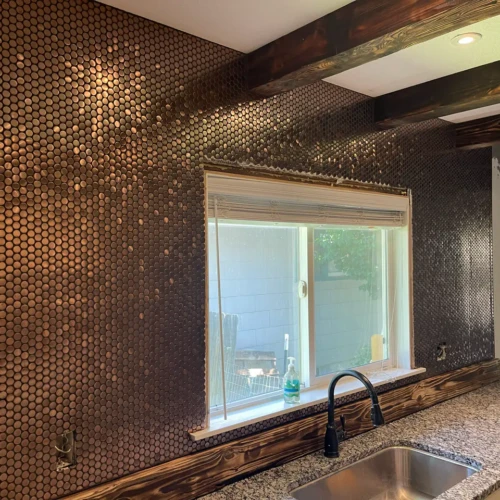 Full-wall kitchen installation of metallic copper penny round mosaic tiles Colorado Springs, CO, surrounding a window and wood beams by XCEL TILE.