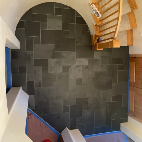 Overhead view of a curved entryway floor finished in dark multi-size natural slate tiles featuring precise radius cuts tracing a staircase in Monument, CO, by XCEL TILE.