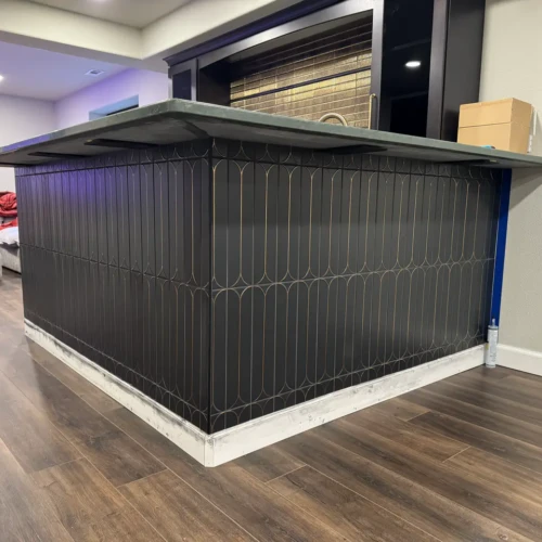 Custom basement bar island featuring dark matte scalloped tile with bright brass metallic inlay wrapping seamlessly around a corner in Colorado Springs, CO, by XCEL TILE.
