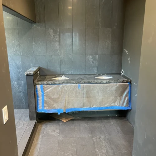 Large dual-sink bathroom in Black Forest, CO, featuring a vanity framed by floor-to-ceiling charcoal stone-look tile backsplash by XCEL TILE.