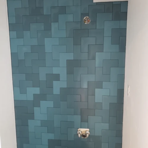 A bold, custom bathroom accent wall in Colorado Springs, CO, featuring an intricate geometric pattern composed of teal and blue rectangular tiles by XCEL TILE.