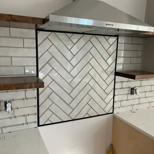 Kitchen remodel under construction showcasing a light grey herringbone tile accent wall perfectly framed beneath a stainless steel vent hood, flanked by standard subway tileTall, multi-tiered custom shower niche built into a light grey subway tile wall, featuring a light herringbone tile backer and white quartz shelves in Monument, CO, by XCEL TILE.