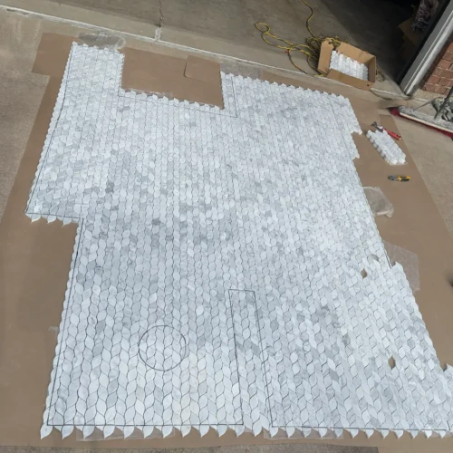 Intricate white and grey marble leaf-pattern mosaic tile sheets laid out and templated on a garage workspace floor in Colorado Springs, CO, by XCEL TILE.