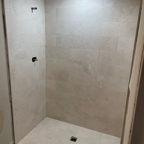 Finished walk-in shower enclosure in Colorado Springs, CO, completely clad in large-format, light marble-look stone tile on the walls and floor by XCEL TILE.