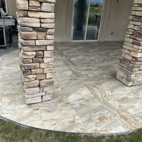 Close-up of large-format outdoor stone-look porcelain patio tiles in Peyton, CO, meeting custom stacked stone support columns by XCEL TILE.