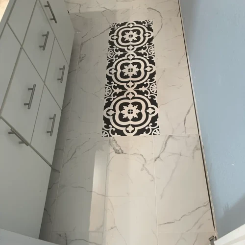 White marble-look bathroom floor tile in Colorado Springs, CO, featuring a striking custom inlay of black and white patterned decorative tile by XCEL TILE.