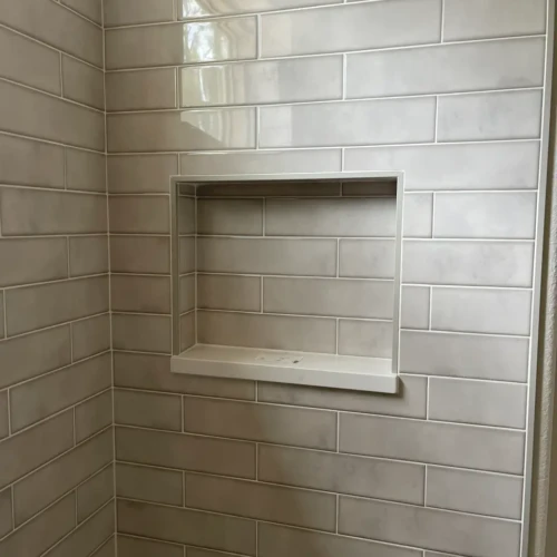 Close-up of a custom recessed shower niche built into a light grey subway tile wall, framed by a bright brass metallic edge trim in Parker, CO, by XCEL TILE.