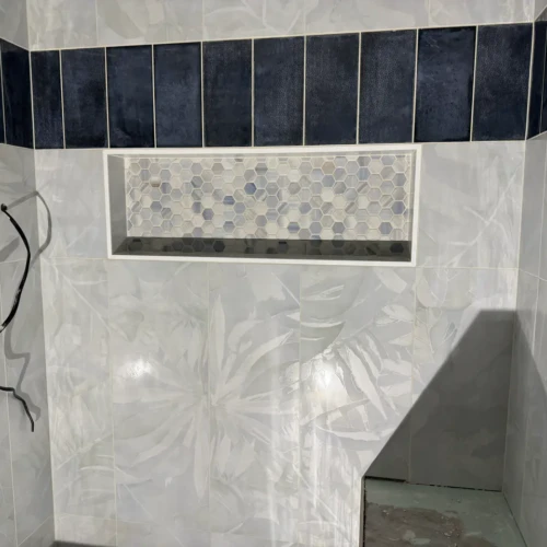 Close-up of a custom wide shower niche filled with hexagon mosaic tiles, positioned seamlessly below a band of dark navy vertical accent tiles in Manitou Springs, CO, by XCEL TILE.