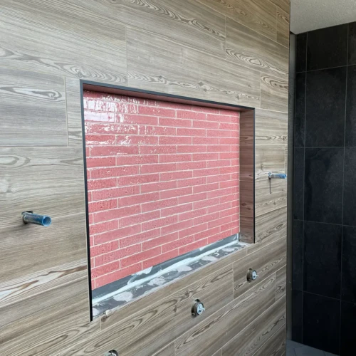 Shower wall under construction in Castle Rock, CO, showcasing wood-look tile, exposed plumbing rough-ins, and a massive recessed niche featuring bright pink subway tile by XCEL TILE.